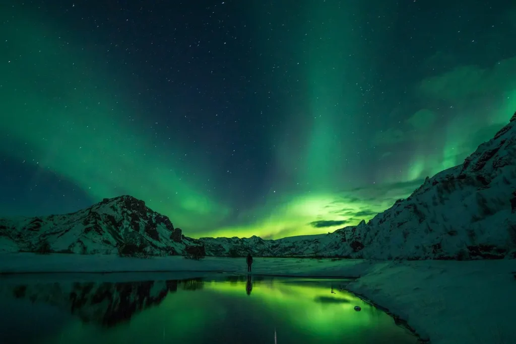 Green Aurora Borealis illuminating snow-covered mountains in Iceland at night.